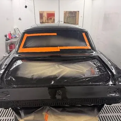 Rear view in the spray booth: fresh black paint, rear window masked with orange tape