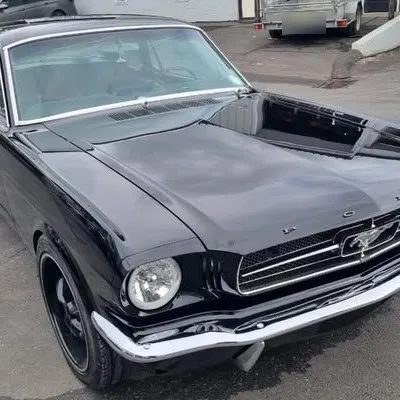 Finished 1965 Mustang in gloss black from the front left, with chrome bumper and pony grille