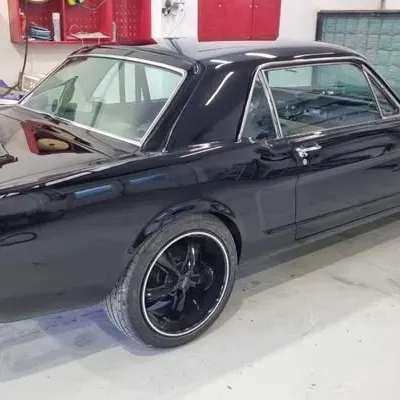 Side profile of the finished Mustang in the workshop: gloss black, chrome trim and black wheels